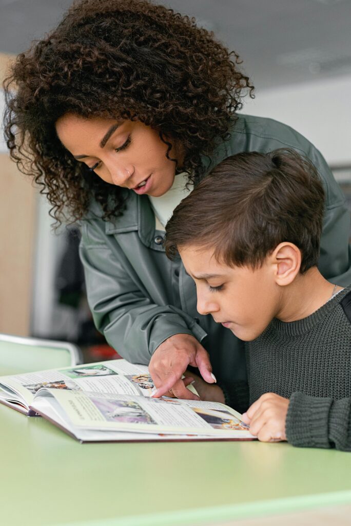A woman helps a boy read in a classroom setting. Educational support concept.